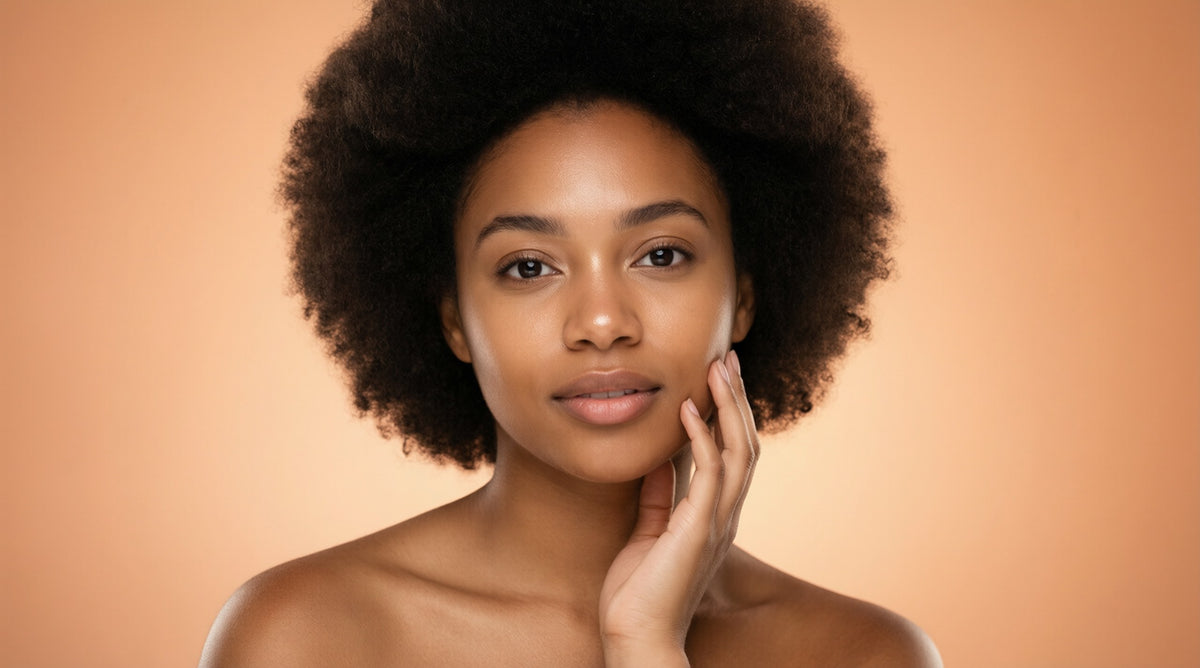 Woman with glowing skin gently touching her face against a warm peach background